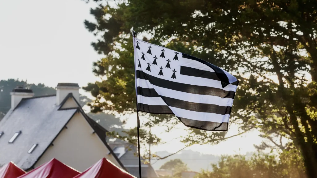 Drapeau breton Gwenn ha Du flottant au-dessus de tentes de festival, devant une maison bretonne