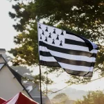 Drapeau breton Gwenn ha Du flottant au-dessus de tentes de festival, devant une maison bretonne